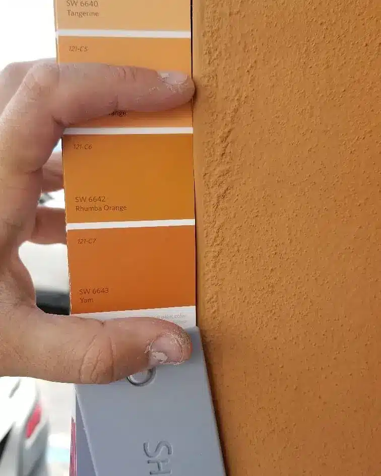 Painter holding Sherwin-Williams orange swatches against sunlit stucco to test Miami paint colors